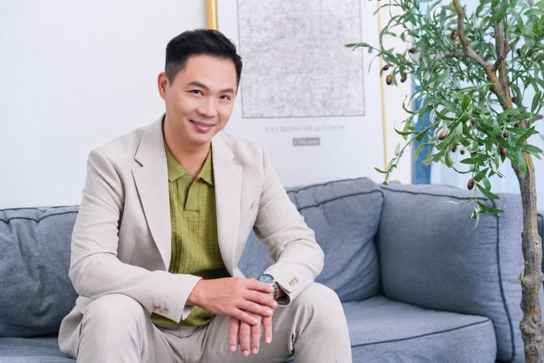 Coach Lin 穿著米色外套,坐在沙發上微笑